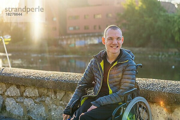 Eine behinderte Person im Rollstuhl neben einem Fluss in der untergehenden Sonne der Stadt