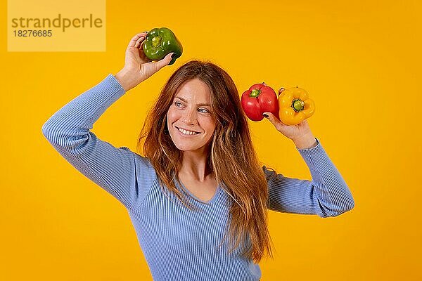 Vegetarische Frau mit grünen  gelben und roten Paprikaschoten auf gelbem Hintergrund  gesunde Ernährung