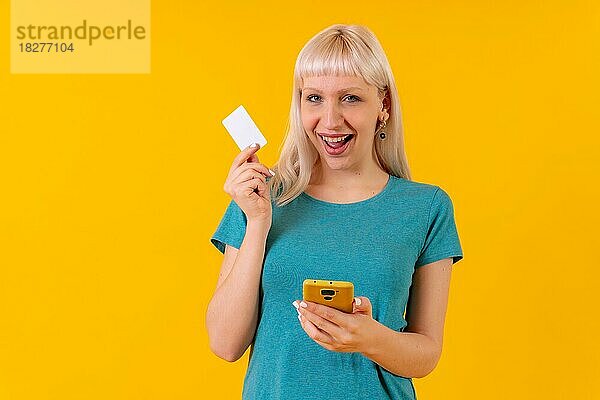 Online-Zahlung mit der Karte auf dem Telefon  blonde kaukasische Mädchen im Studio auf einem gelben Hintergrund