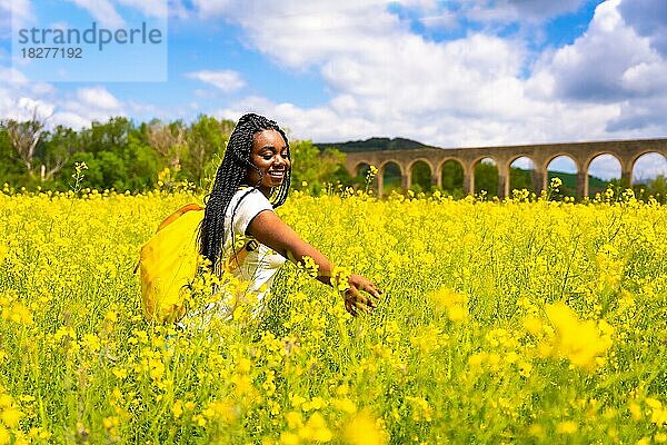 Ein schwarzes ethnisches Mädchen mit Zöpfen  eine Reisende  genießt die Freiheit in einem Feld mit gelben Blumen