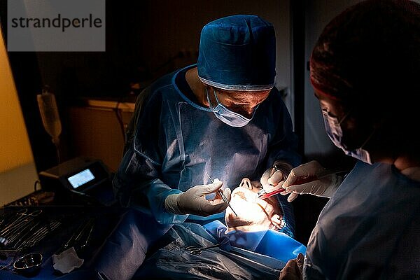 Zahnklinik  Zahnarzt und Assistentin führen im Dunkeln eine orale Operation durch