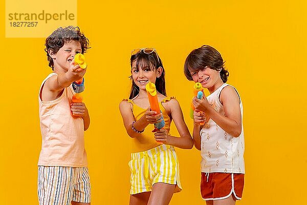 Kinder haben Spaß mit Wasserpistolen im Sommerurlaub  gelber Hintergrund