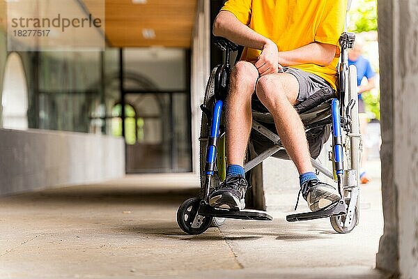 Detail einer behinderten Person in einem Rollstuhl  die neben einigen Säulen in einer Tür lächelt