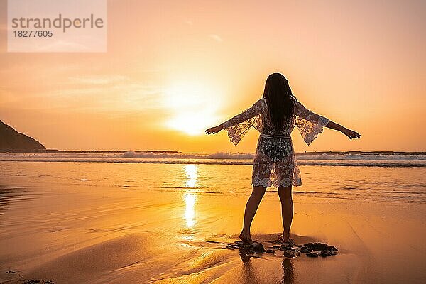 Silhouette einer Frau am Strand bei Sonnenuntergang in einem weißen Kleid