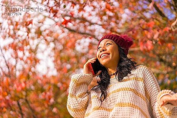 Porträt einer asiatischen Frau im Herbst mit einem Mobiltelefon  das in einem Wald aus roten Blättern telefoniert  Technik