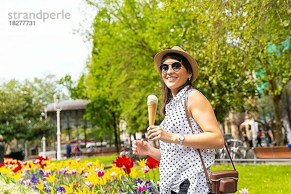 Eine Touristin  die die Stadt besucht  isst eine Eistüte  genießt die Sommerferien und hat eine Kamera dabei  ein weiblicher Alleinreisender  der eine Sonnenbrille und einen Hut trägt