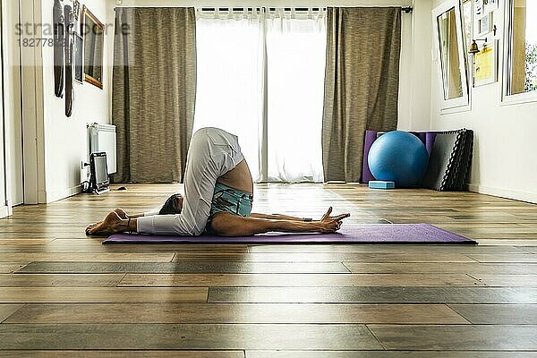 Seitenansicht einer Frau  die Yoga praktiziert und die Taubenstellung (Karnapidasana) einnimmt