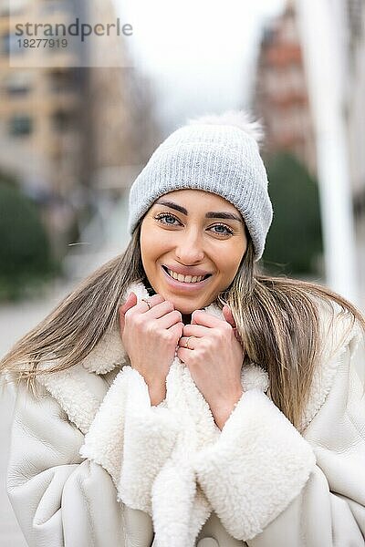 Winterporträt einer kaukasischen Frau mit Wollmütze in der Stadt  lächelnd
