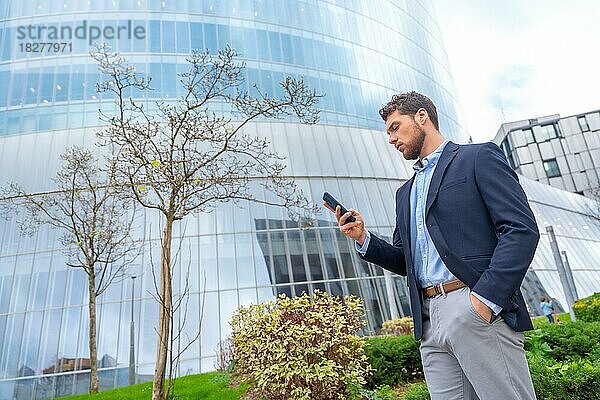 Männlicher Geschäftsmann oder Unternehmer mit Blick auf das Handy außerhalb des Büros  Gewerbegebiet