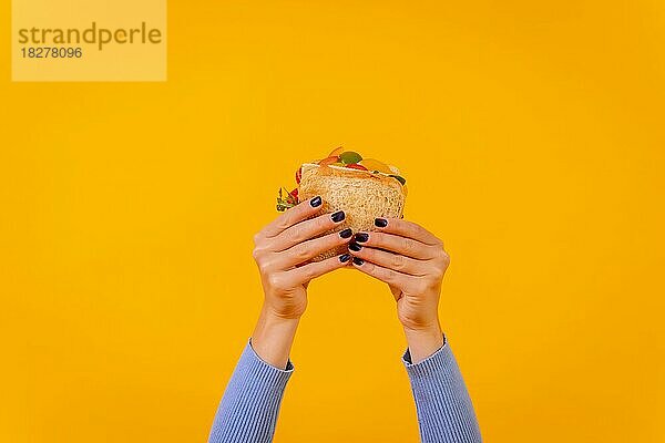 Hände einer Frau mit einem Sandwich auf einem gelben Hintergrund  gesundes Essen