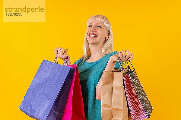 Lächelnd Einkaufen mit Taschen auf Verkauf  blonde kaukasische Mädchen im Studio auf gelbem Hintergrund