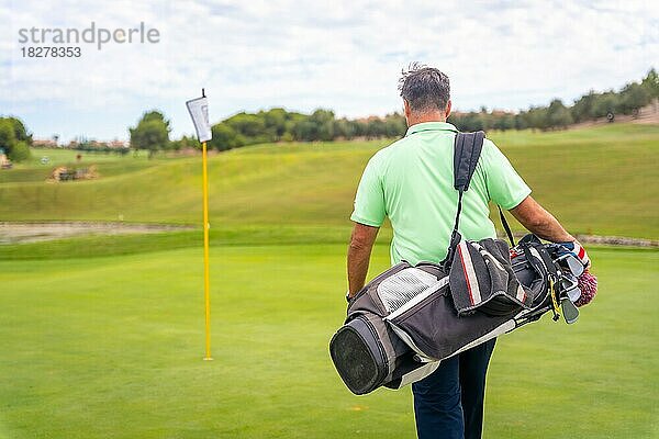 Porträt eines männlichen Golfspielers  der mit seinen Taschen das Fairway entlangläuft und Golf spielt