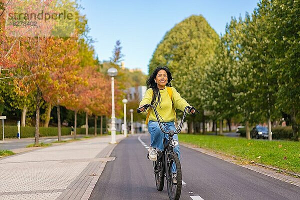 Junge asiatische Studentin auf dem Fahrrad auf dem Weg zur Universität entlang des Radwegs  gesundes Leben  umweltfreundlich