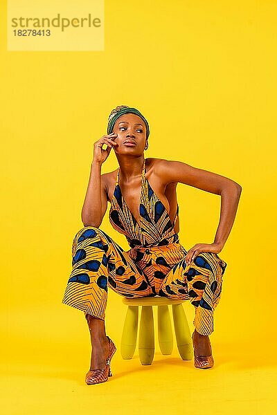 Junge afrikanische Frau in traditioneller Kleidung auf gelbem Hintergrund  sitzend  Werbefotografie
