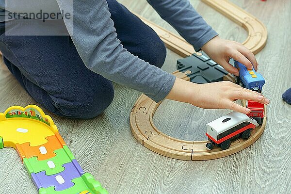 Kind  das mit einer Holzeisenbahn auf dem Boden in seinem Zimmer spielt