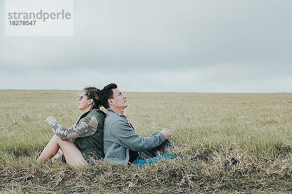 Verliebtes Paar auf dem Feld  Rücken an Rücken sitzend und in den Himmel blickend  Junges entspanntes Paar  das mit dem Rücken zueinander auf dem Feld sitzt und in den Himmel blickt