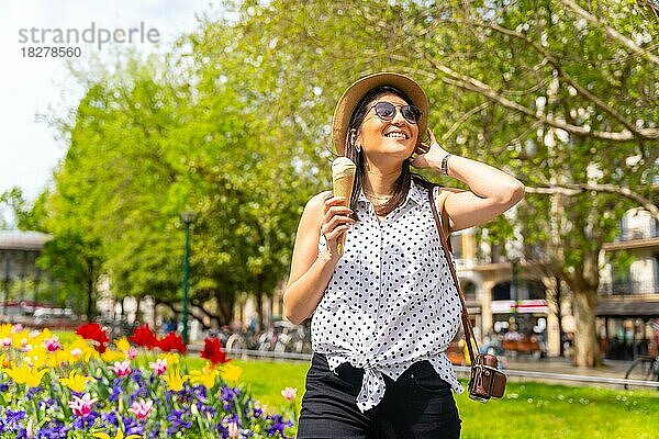 Eine touristische Frau  die die Stadt besucht  isst eine Eistüte  genießt die Sommerferien und hat eine Kamera dabei  ein weibliches Solo-Reisekonzept  trägt eine Sonnenbrille