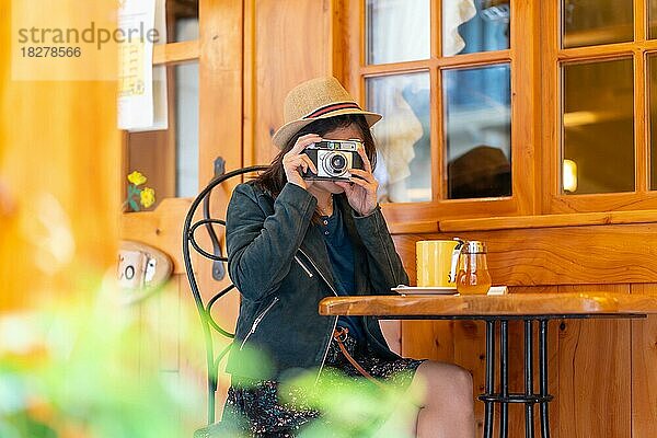 Ein Touristenmädchen mit Hut und Fotoapparat trinkt Tee auf einer Caféterrasse und macht Fotos von ihrem Urlaub