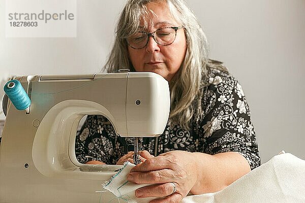 Ältere Frau mit weißem Haar  unscharf  näht einen weißen Stoff auf einer Nähmaschine