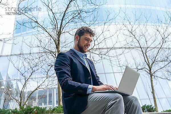 Junger Geschäftsmann oder Finanzmann  der vor einem Büro auf einen Computer schaut  Glasgebäude