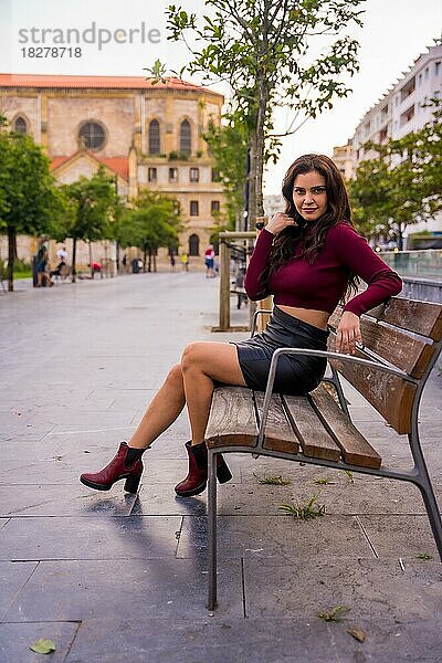 Brünette Frau im Lederrock sitzend in der Stadt  Lifestyle  Mode-Pose  vertikales Foto