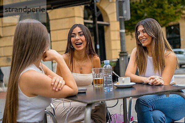 Porträt junger Freundinnen  die an einem Nachmittag auf der Terrasse einer Cafeteria im Herbst etwas trinken