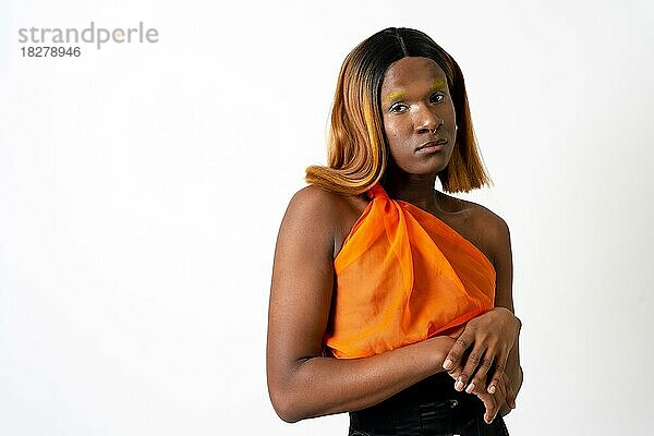 Schwarzer ethnischer Mann in einem Studio  LGTBI-Konzept  Porträt mit orangefarbenem Kleid und Perücke