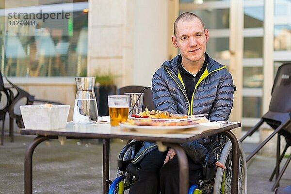 Eine behinderte Person im Rollstuhl in einem Restaurant  die auf ihr Essen wartet