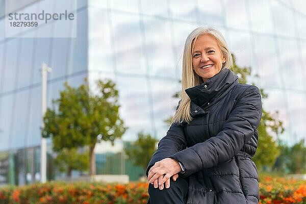 Unternehmensporträt einer lächelnden Geschäftsfrau mittleren Alters in der Nähe eines Wolkenkratzers