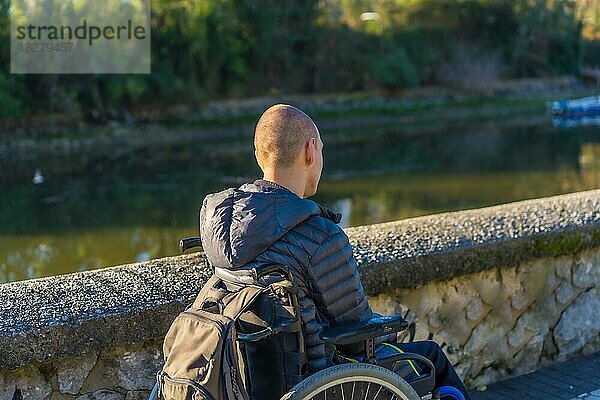 Eine behinderte Person im Rollstuhl in einem Park bei Sonnenuntergang am Fluss