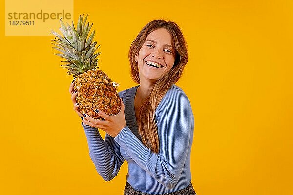 Mädchen lächelnd mit einer Ananas in Sonnenbrille in einem Studio auf einem gelben Hintergrund  gesund  Sommer