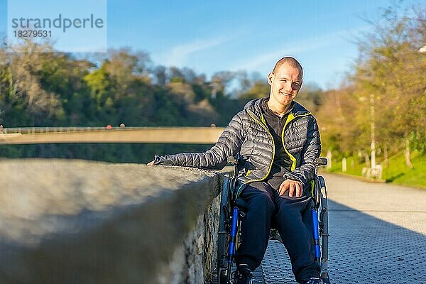 Eine behinderte Person in einem Rollstuhl in einem Park bei Sonnenuntergang neben einem Fluss bei Sonnenuntergang