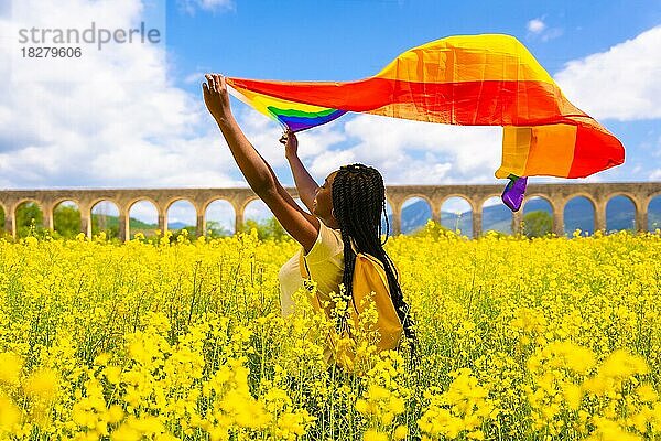 Ein schwarzes ethnisches Mädchen mit Zöpfen hält die LGBT-Flagge in einem Blumenfeld