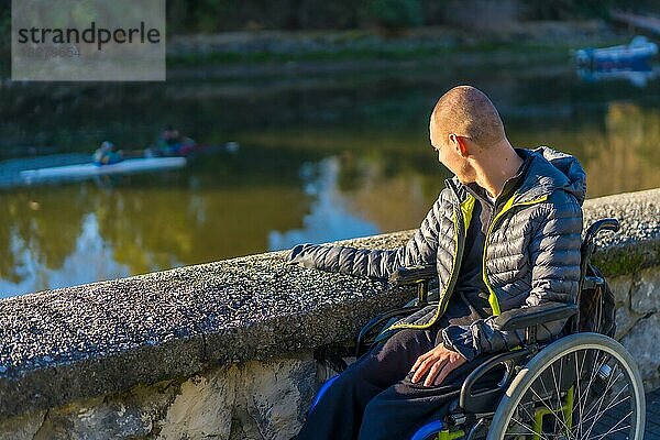 Eine behinderte Person im Rollstuhl in einem Park mit Blick auf den Fluss