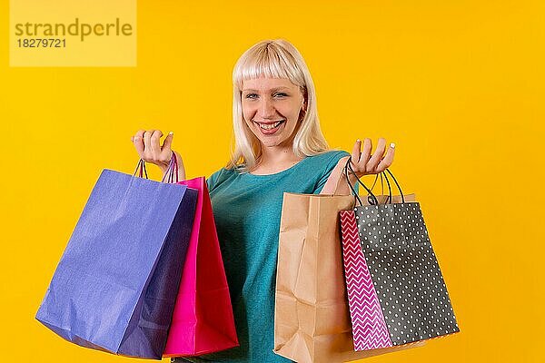 Lächelnd Einkaufen mit Taschen auf Verkauf  blonde kaukasische Mädchen im Studio auf gelbem Hintergrund