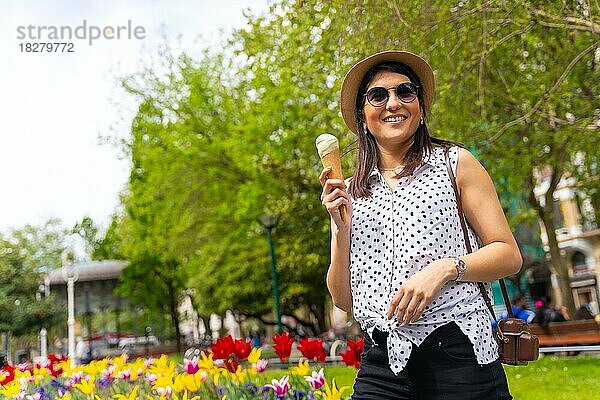 Eine touristische Frau  die die Stadt besucht  isst eine Eistüte  genießt die Sommerferien und hat eine Kamera dabei  ein weibliches Solo-Reisekonzept  trägt eine Sonnenbrille