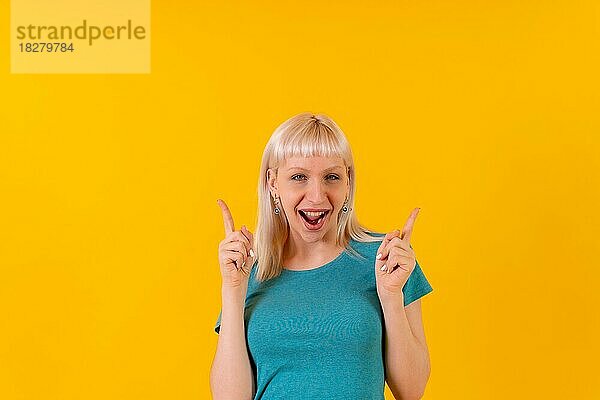 Porträt lächelnd nach oben zeigend  blondes kaukasisches Mädchen im Studio auf gelbem Hintergrund