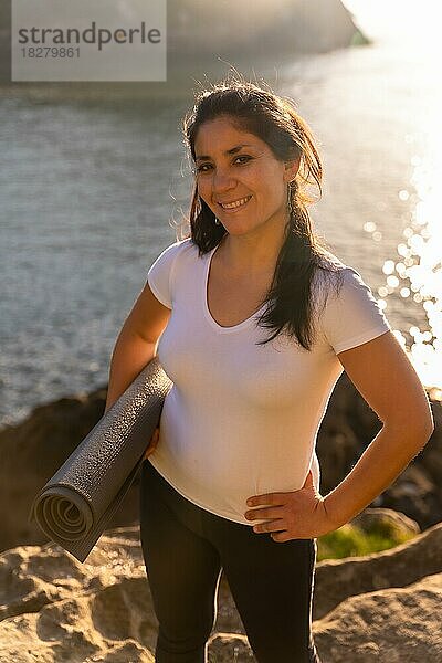 Eine Frau macht Yoga in der Natur am Meer  posiert mit der Matte  gesundes und naturistisches Leben  Pilates im Freien