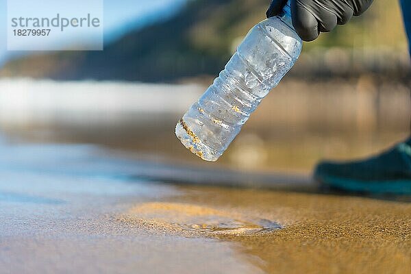 Hand einer nicht erkennbaren Person  die Müll oder Plastik am Strand aufsammelt