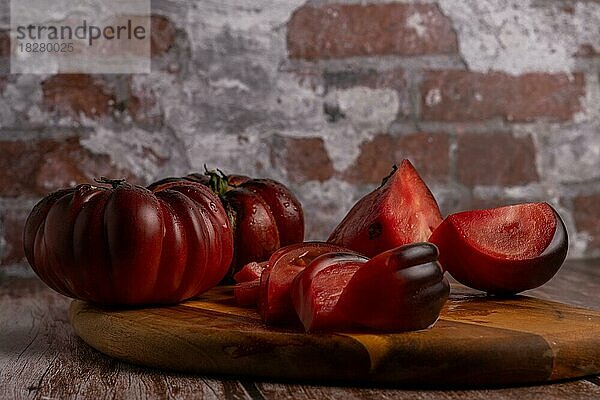 Gruppe von geschnittenen und ganzen maurischen Bio-Tomaten auf einem Holzbrett mit einer Backsteinmauer im Hintergrund