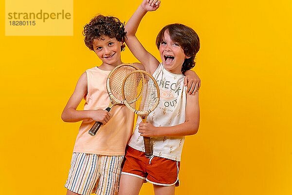 Porträt von zwei Brüdern  die im Sommerurlaub Tennis spielen und Spaß haben  gelber Hintergrund