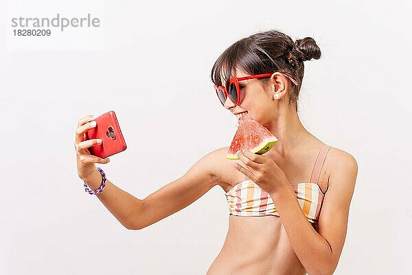 Mädchen mit Sonnenbrille genießt den Sommer  isst eine Wassermelone und macht ein Selfie mit dem Telefon. Weißer Hintergrund