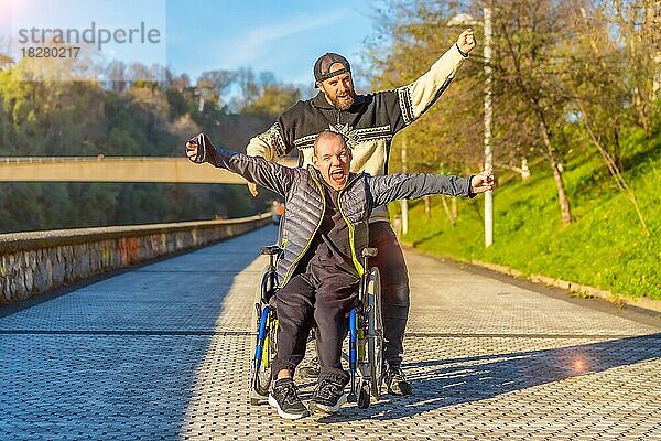 Behinderte Person im Rollstuhl mit Freund überglücklich  lächelnd  genießen mit Armen oben  vistoria  genießen das Leben im Sonnenuntergang der Stadt