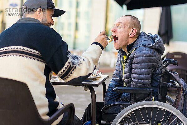 Eine behinderte Person isst mit Hilfe eines Freundes und hat Spaß  Terrasse eines Restaurants
