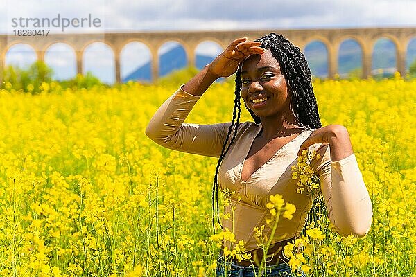Lebensstil  Porträt eines schwarzen ethnischen Mädchens mit Zöpfen  das in die Kamera schaut  Trap-Musik-Tänzerin  in einem Feld mit gelben Blumen