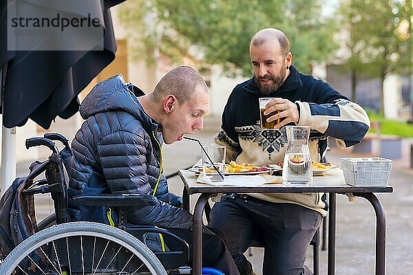 Eine behinderte Person  die mit einem Freund auf der Terrasse eines Restaurants isst und Spaß hat