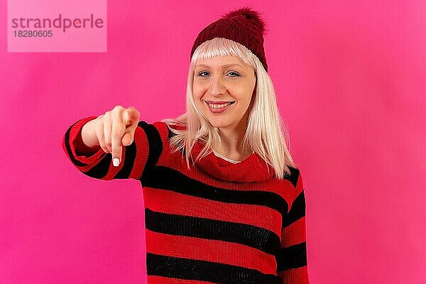 Blonde kaukasische Mädchen auf rosa Hintergrund Studio  Winter-Thema  lächelnd zeigt auf die Kamera