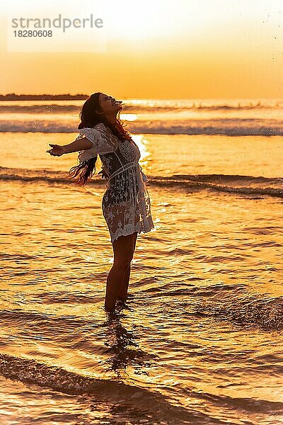 Eine Frau im Sonnenuntergang mit einem weißen Kleid genießt das Meerwasser