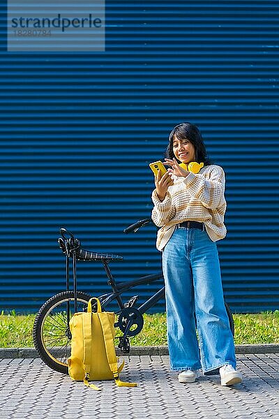 Asiatisches College-Mädchen  das mit gelben Kopfhörern auf einem blauen College-Hintergrund Musik hört