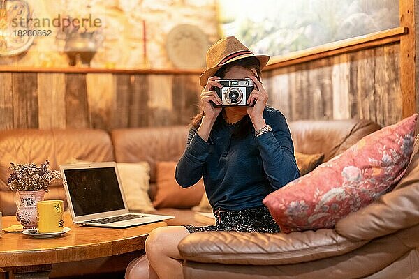 Eine hübsche Touristin mit Hut und Fotoapparat trinkt eine Tasse Tee in einem Café und macht Fotos mit der alten Kamera